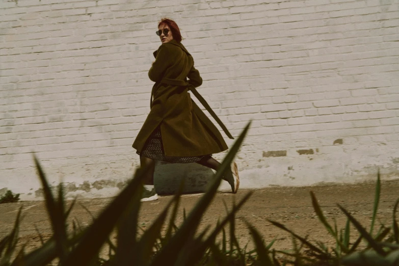 a woman walking down a street in a coat and sunglasses