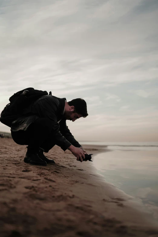 a man crouches over the beach to smell his purse