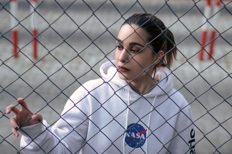 a woman looking through a fence holding her finger up