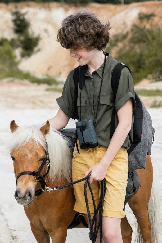 a boy riding on top of a brown horse next to a dirt road