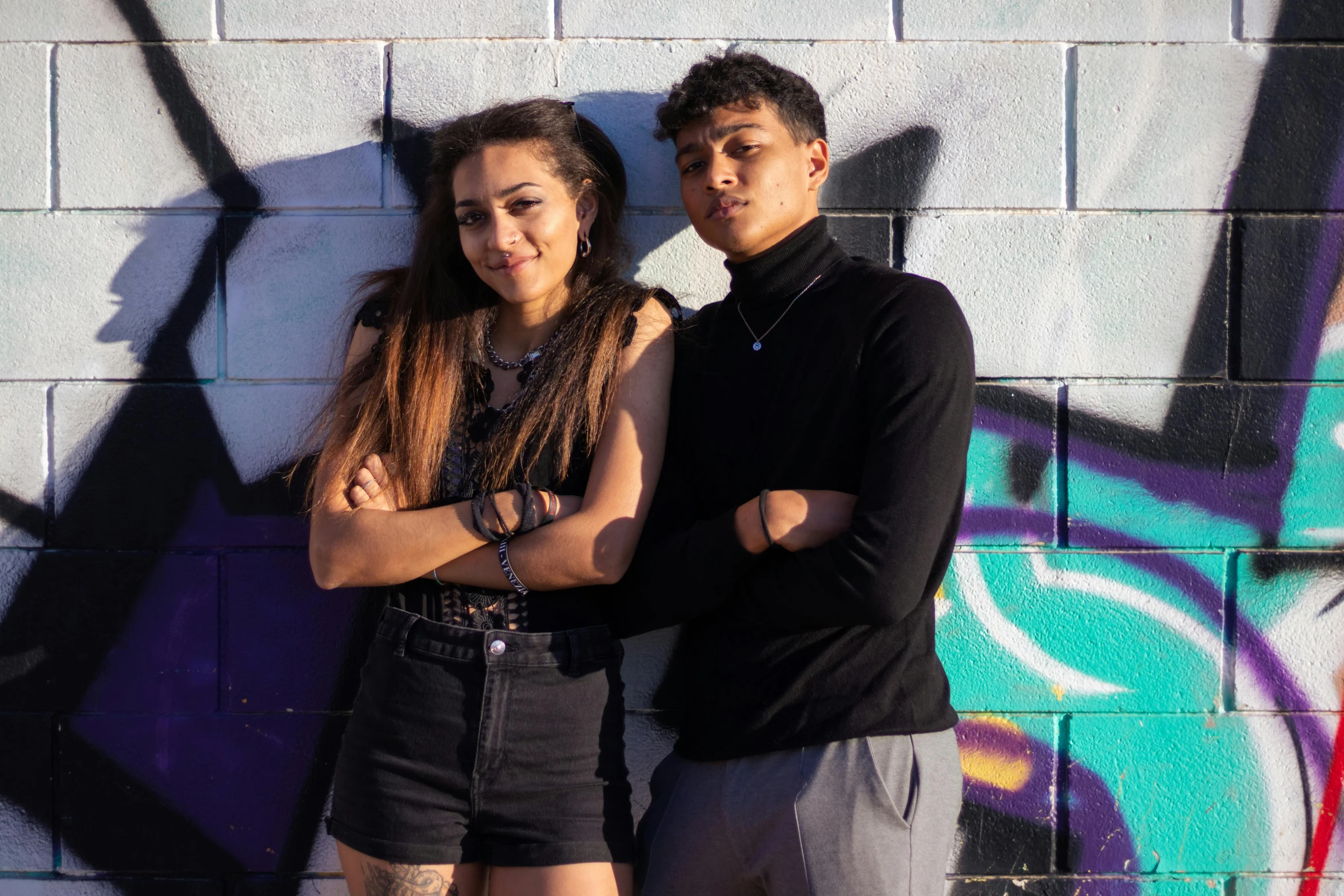 a young man and woman pose for the camera against a wall covered with graffiti