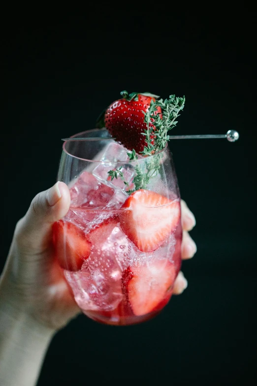 someone is holding a glass with strawberries in it