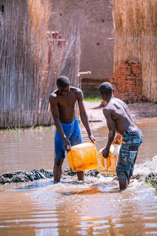 two men standing in water carrying a yellow container