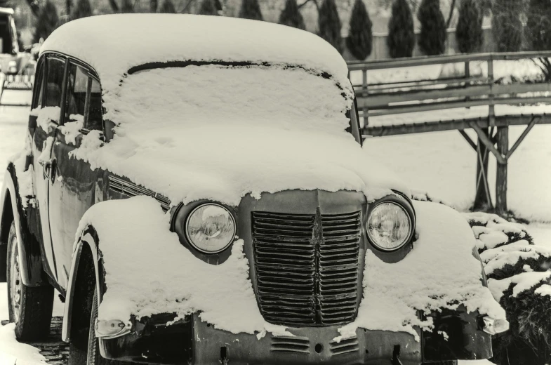 an old car covered with snow parked in front of a fence
