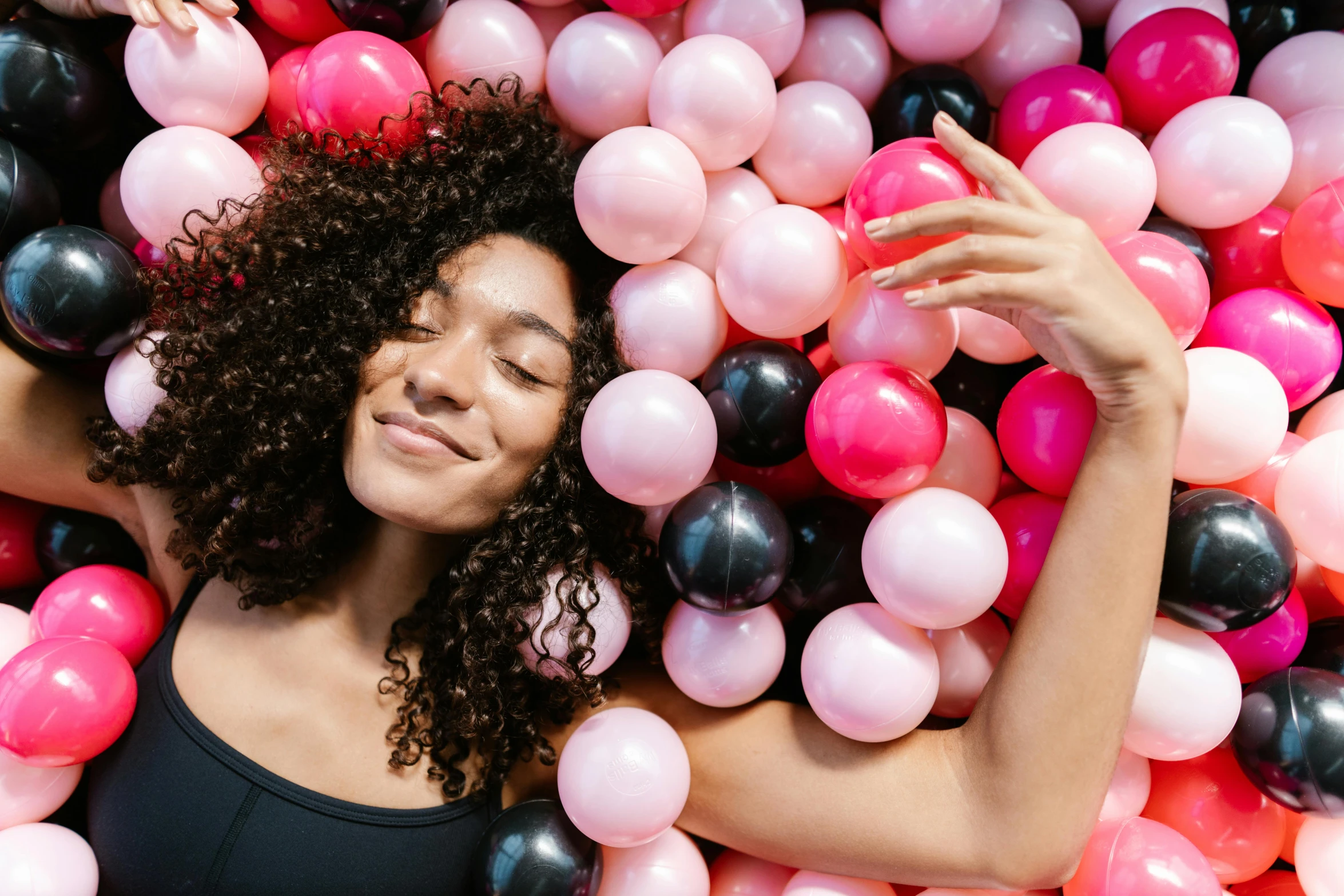 a woman in black bathingsuit lying in a pile of balloons