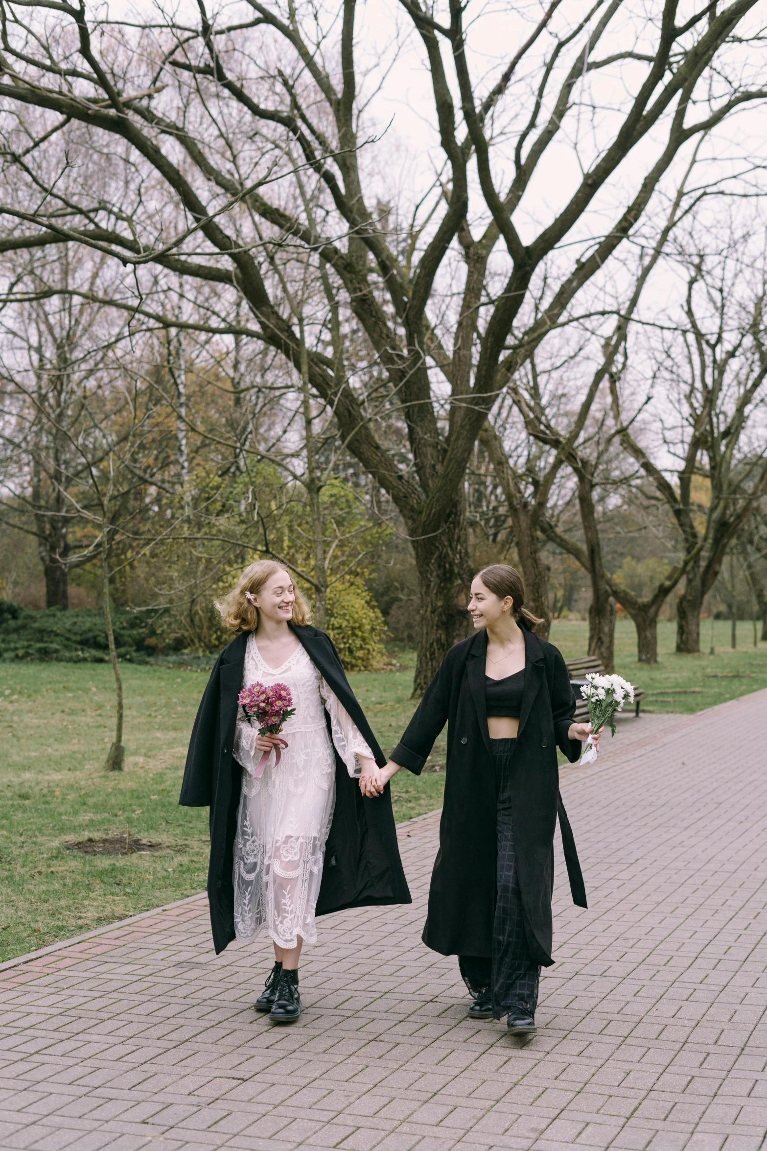 two women dressed in black walking across a brick walkway