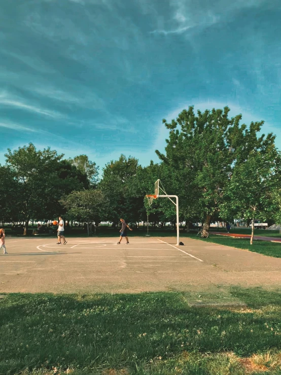 group of people playing basketball on a court with green grass and trees