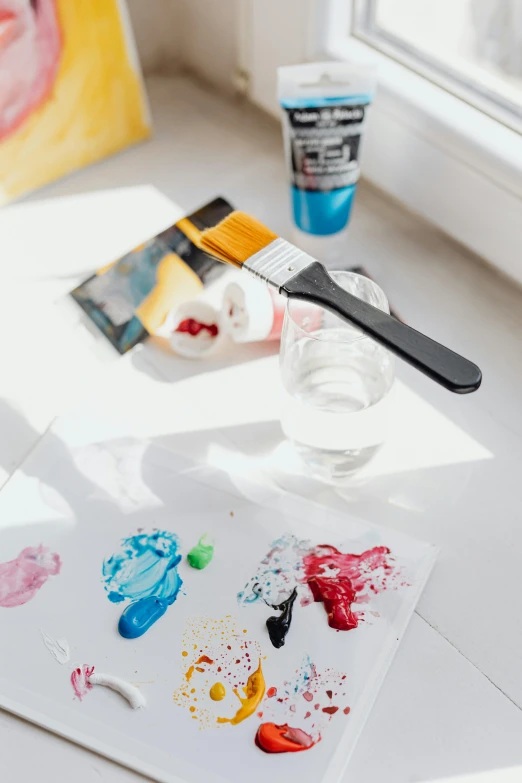 various paints, brushes and cups sitting on the floor