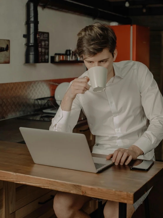 a man drinks coffee while using his laptop