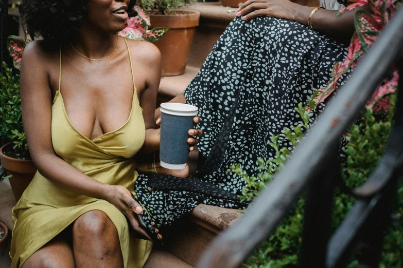 a woman sitting on the steps holding a cup and looking at another woman