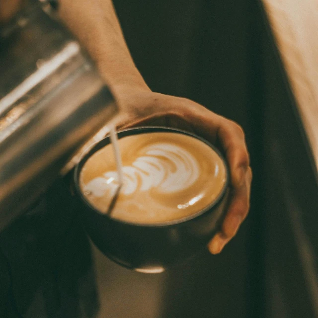 a person holds onto the bowl of a cappuccino