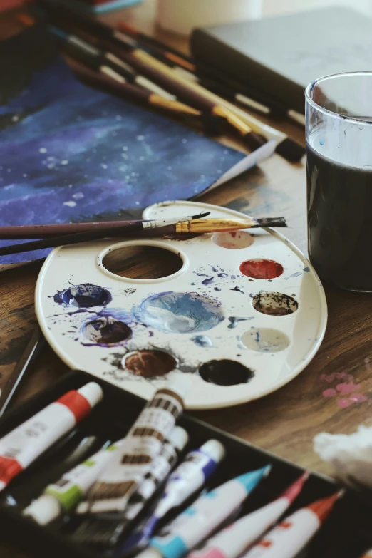 paint and markers are on a table next to a cup