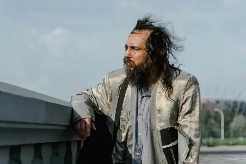 a bearded man with long hair leaning on a fence