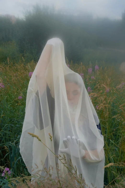 a woman wearing a veil walks through tall grass