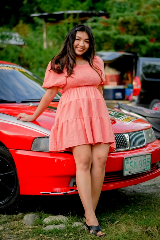 the woman stands next to her car, wearing a pink dress