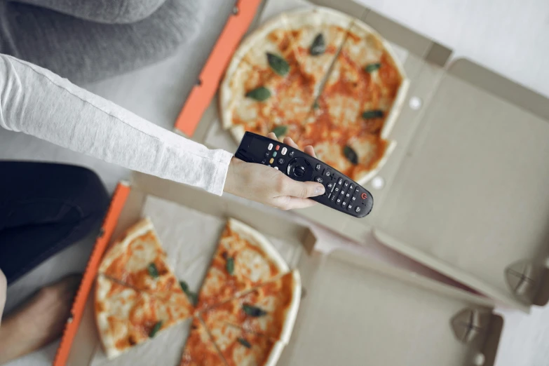 an unrecognizable person holding three pizzas on the ground