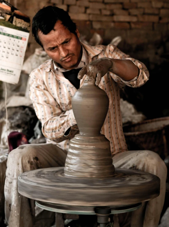 man sitting at table making clay pottery using machine