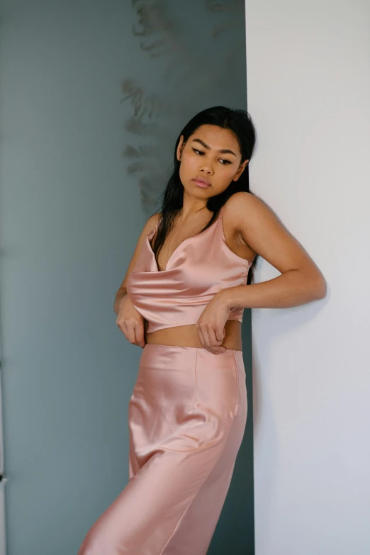 young woman leaning against a wall in a pink long dress