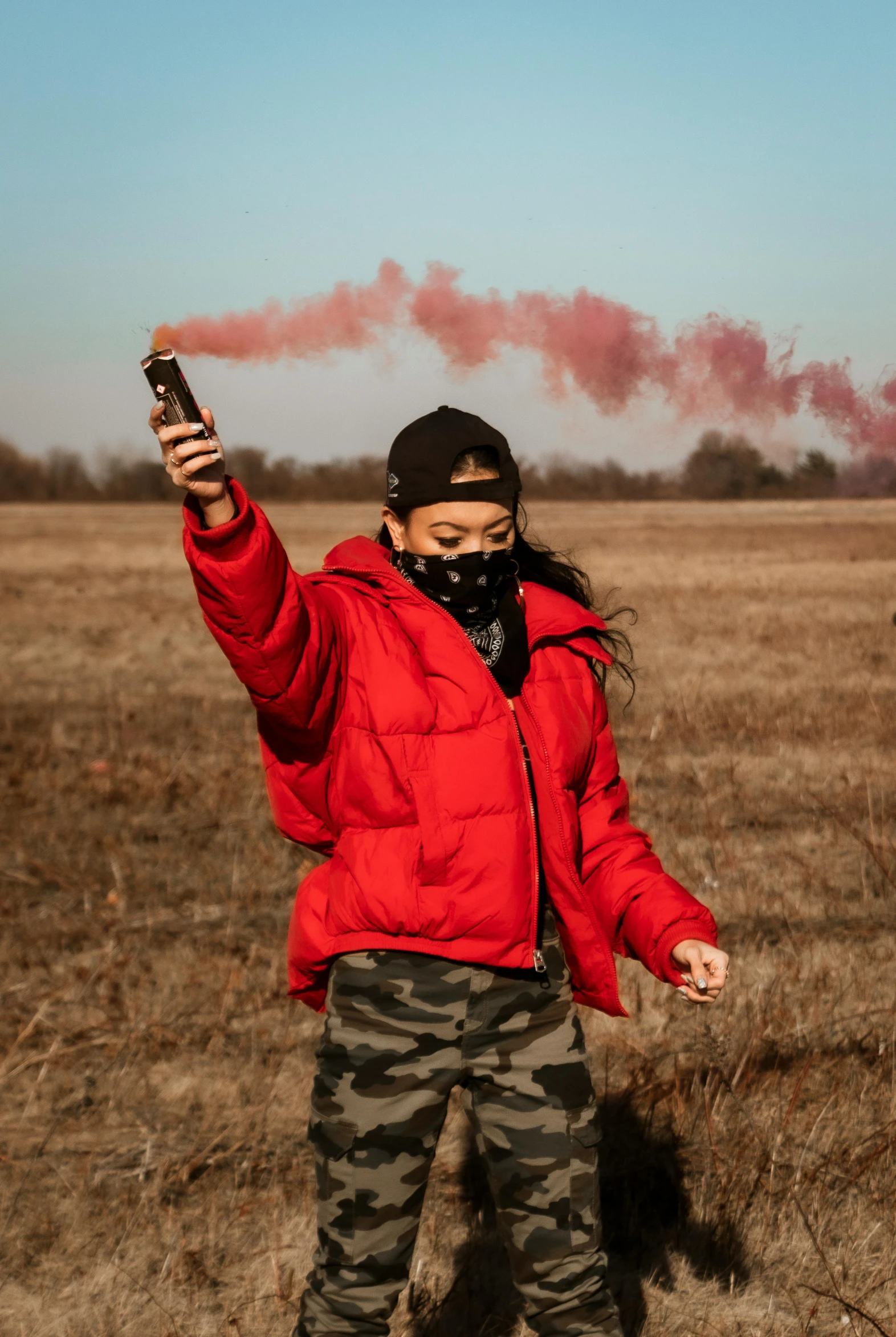 a young person with a cold drink and wearing an orange jacket stands in a field