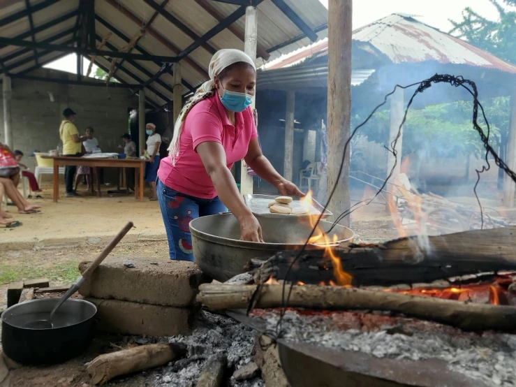 a woman in pink shirt and helmet cooking on fire pit