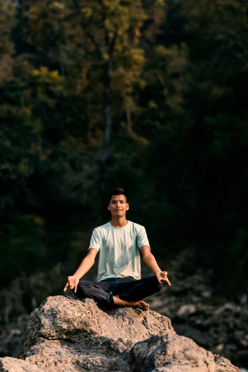 a man sitting on top of a large rock doing yoga