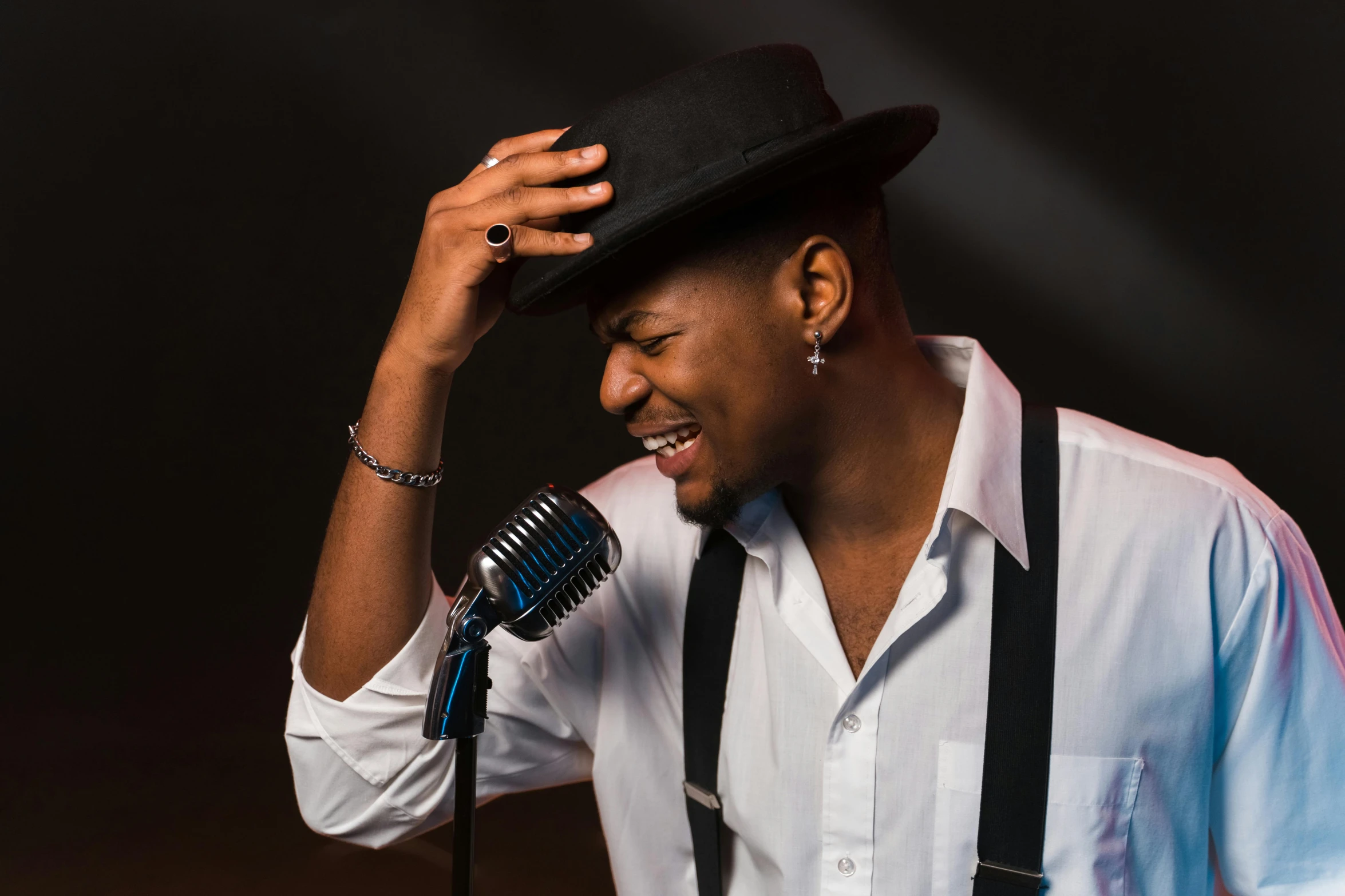 a man in a hat and suspenders holding his head in his hands, while holding onto a microphone