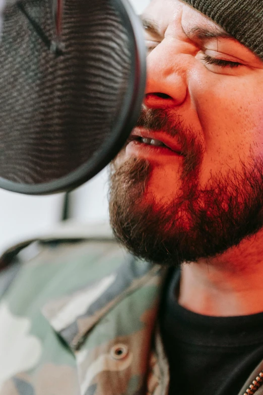 a bearded man wearing a beanie singing into a microphone