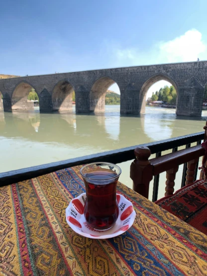 a cup and saucer with a drink on a colorful mat with bridge spanning the river