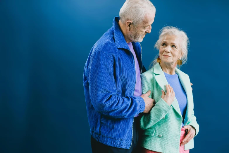 an old man standing next to his wife in front of a blue backdrop