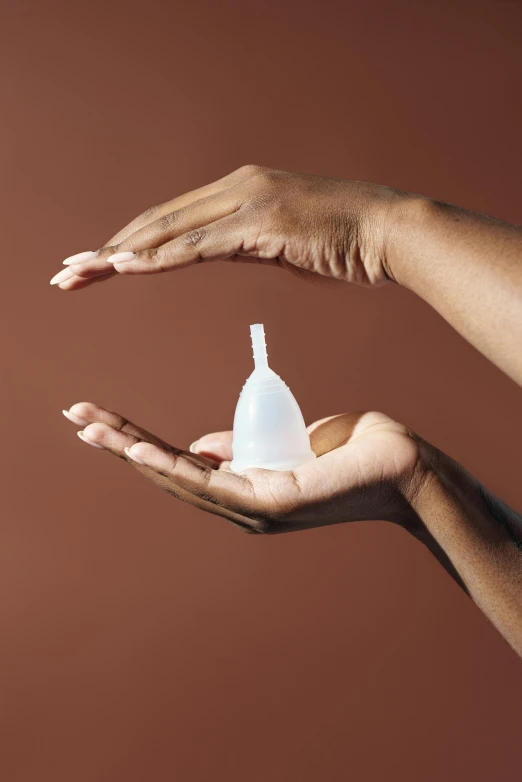 two hands, one holding a bottle of sanitizer on brown background