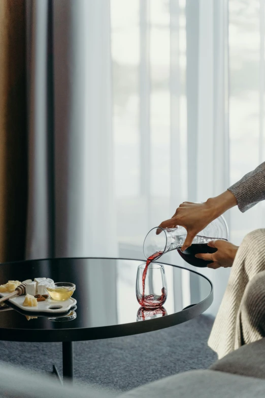 a woman holding a glass with a wine bottle and a vase on top of the table