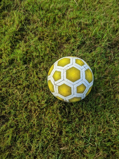 a yellow and white soccer ball sitting on top of a green field