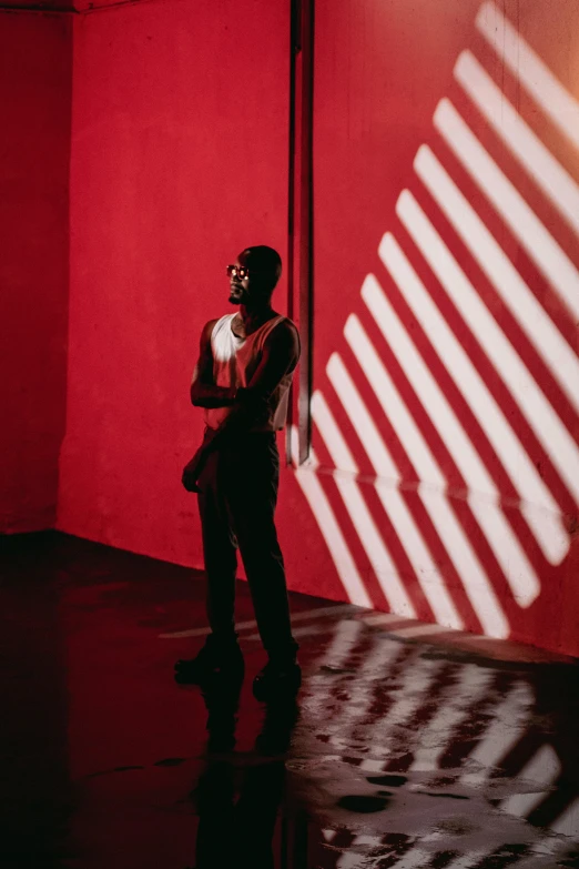 man in suit stands in the shade of a red wall