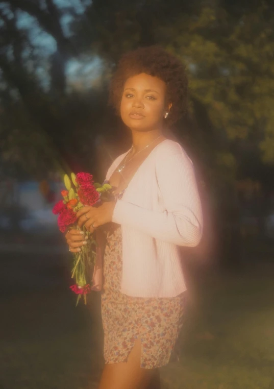 a woman holding flowers in her hands on top of a grass field