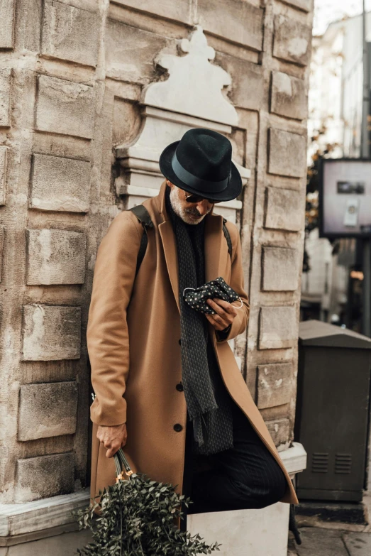 a man dressed in brown and black texting on his cellphone