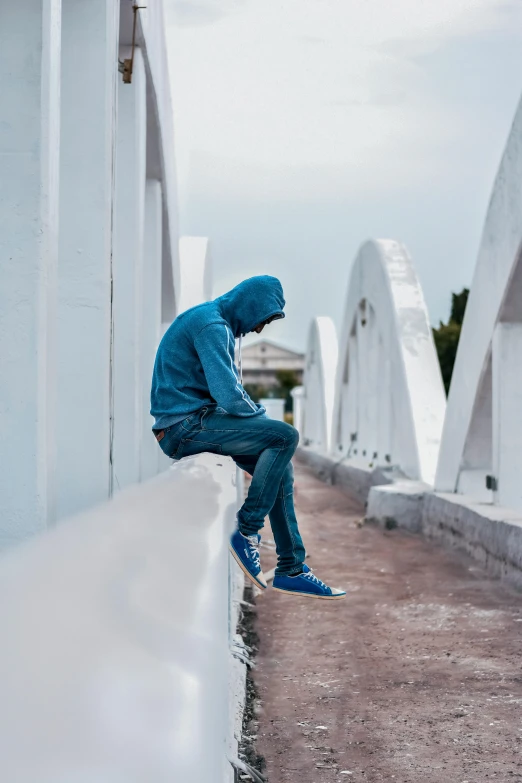 a person in blue jacket leaning against wall with skateboard