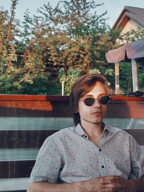 a man wearing glasses sitting on a bench near a swimming pool