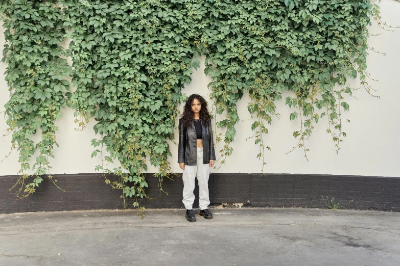 a woman standing next to an ivy covered wall
