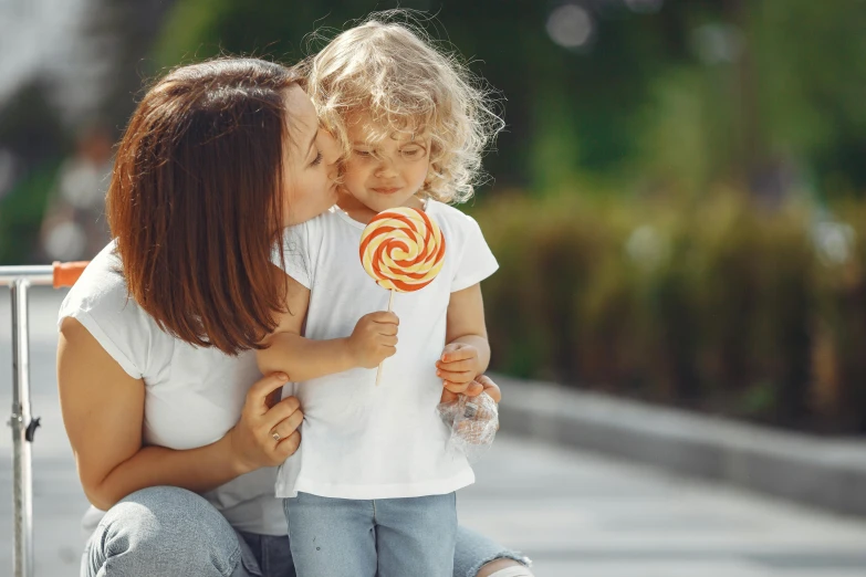 a woman holding her toddler girl holding a lollipop