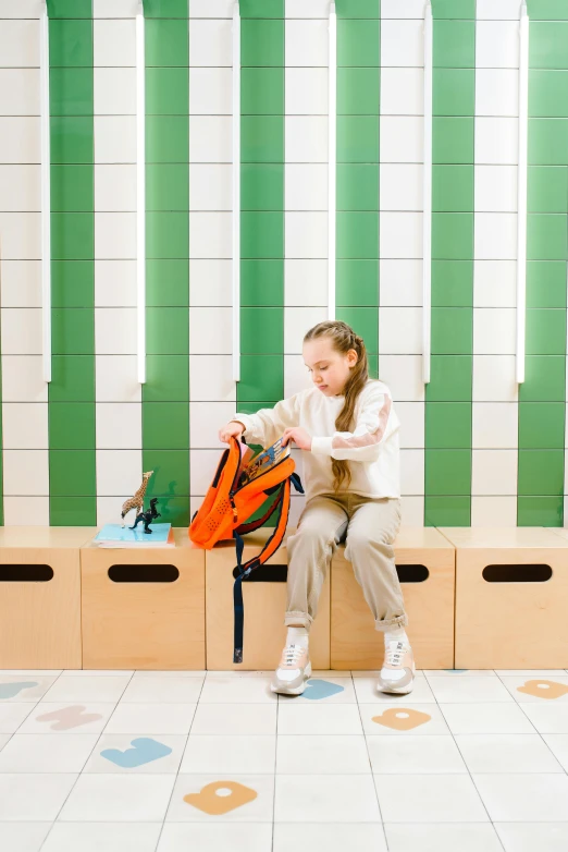 girl with orange backpack sitting on chair in green room