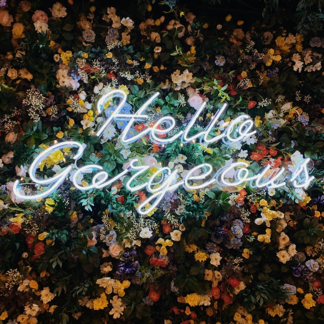 a lit neon sign reading hello gorgeous surrounded by yellow flowers