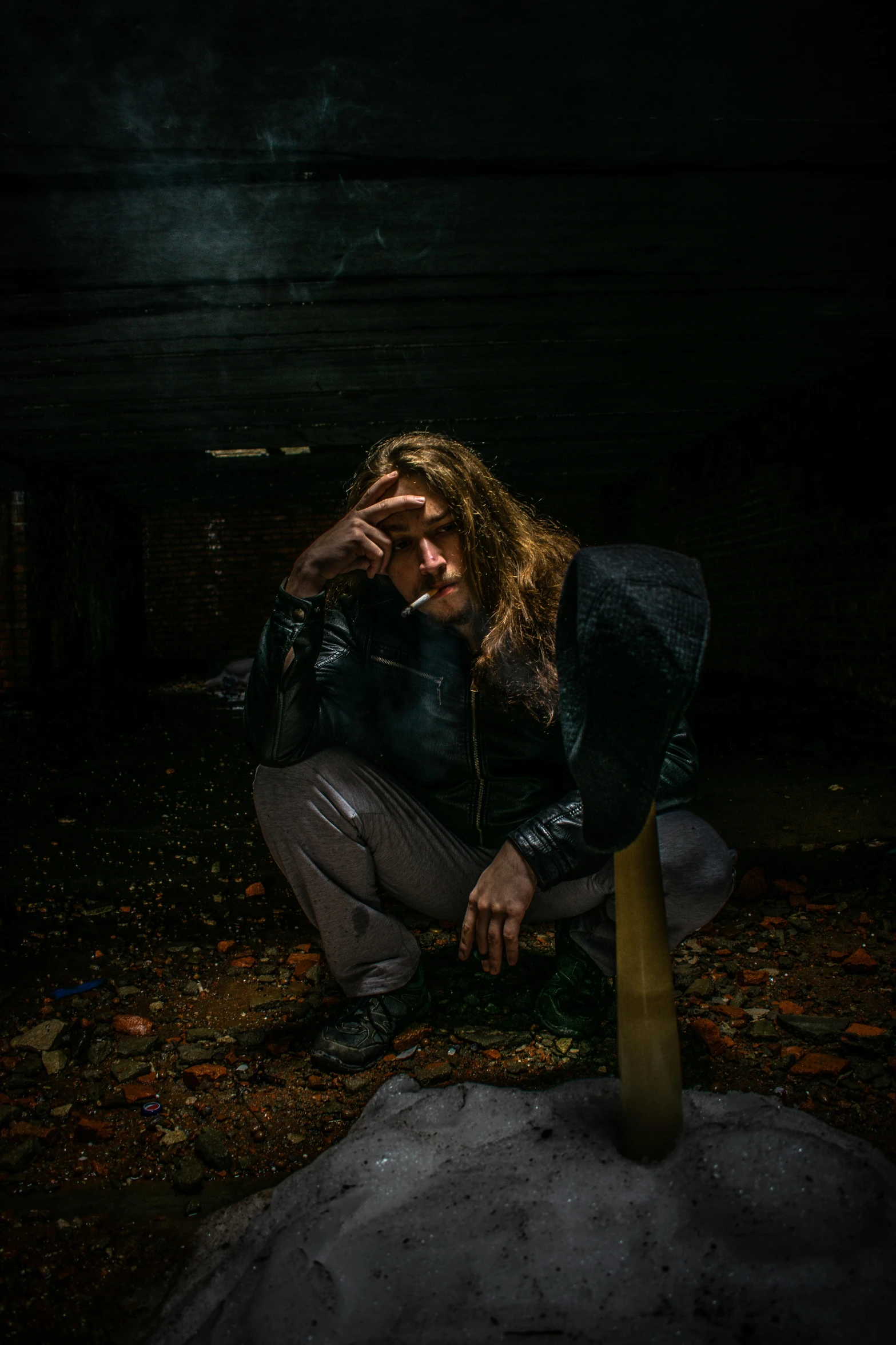 a dark man sitting on the floor in the dark with his arm propped up to his head