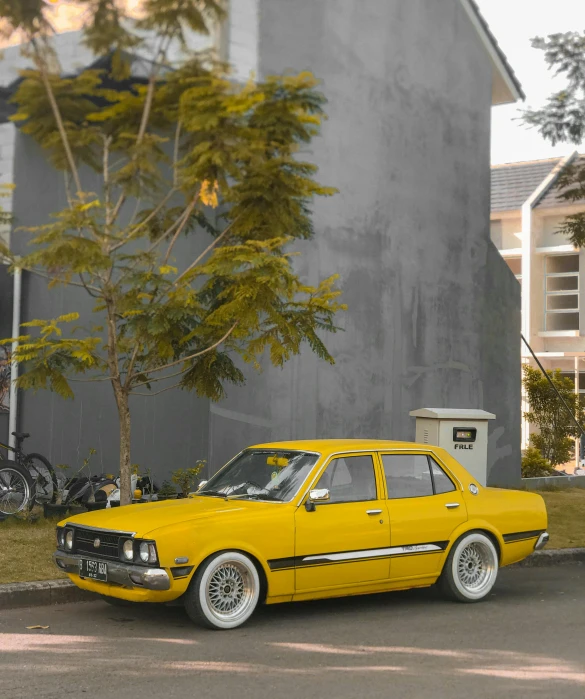 a yellow car parked on the side of a road near a tree