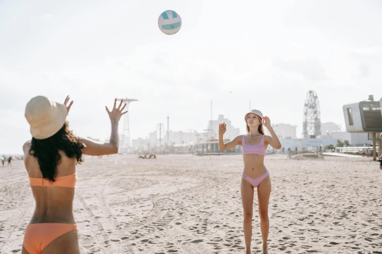 two women wearing hats are on the beach and playing ball