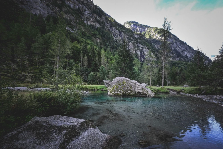 a pond with rocks and grass surrounded by mountains