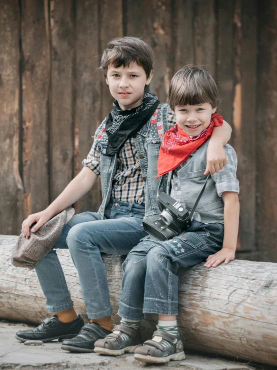 two little boys sitting on a log in a rural setting