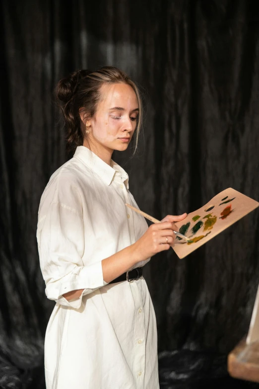 the young woman is standing in front of an easel holding some paintings