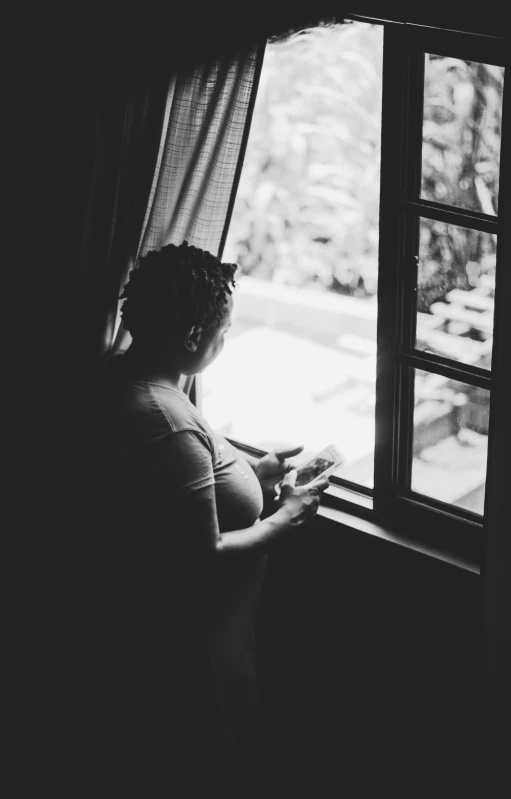 a pregnant woman looks out a window at a house