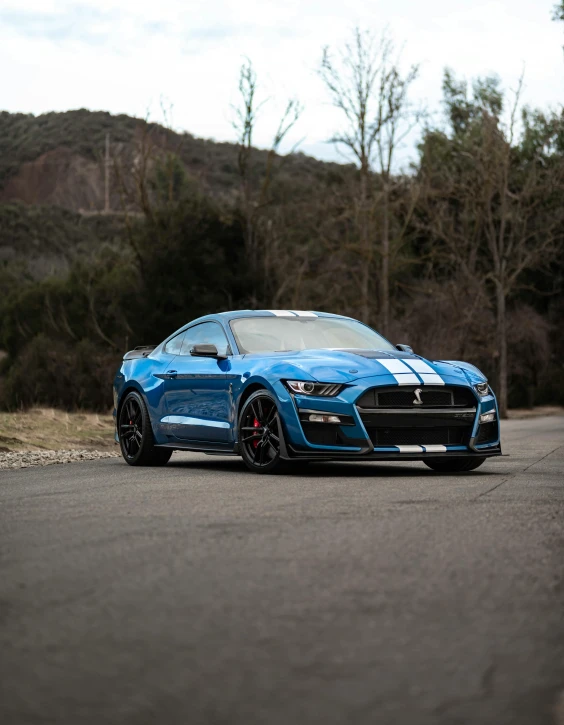 a blue sports car driving down a road next to some forest