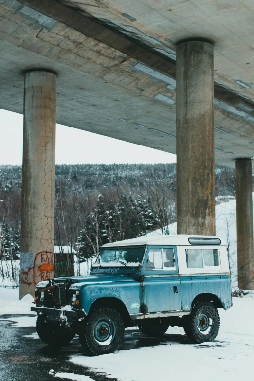 an old car under a bridge on a snowy day